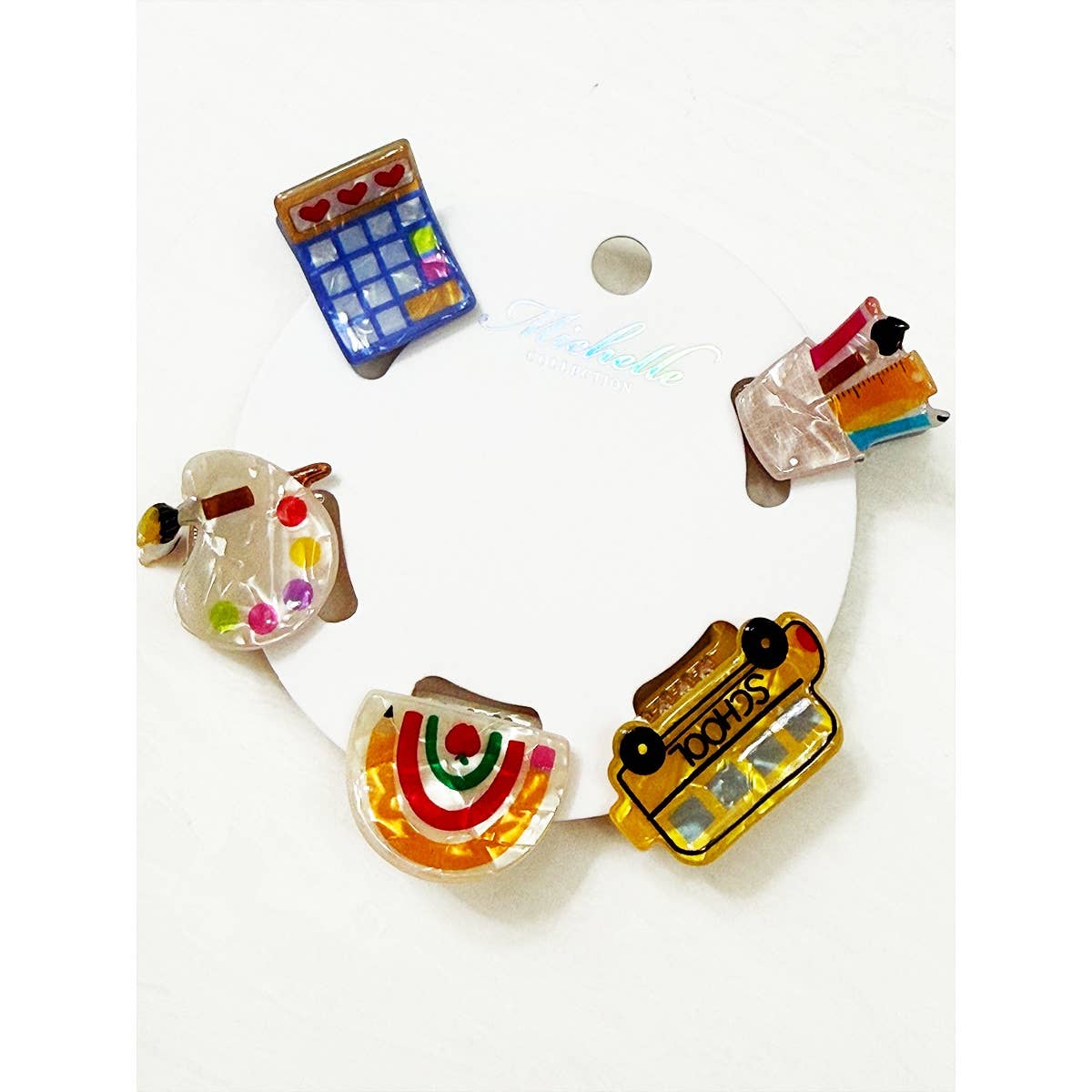 Set of colorful school themed hair clips including a school bus, rainbow, calculator, pencil holder, and paint palette on a white background.