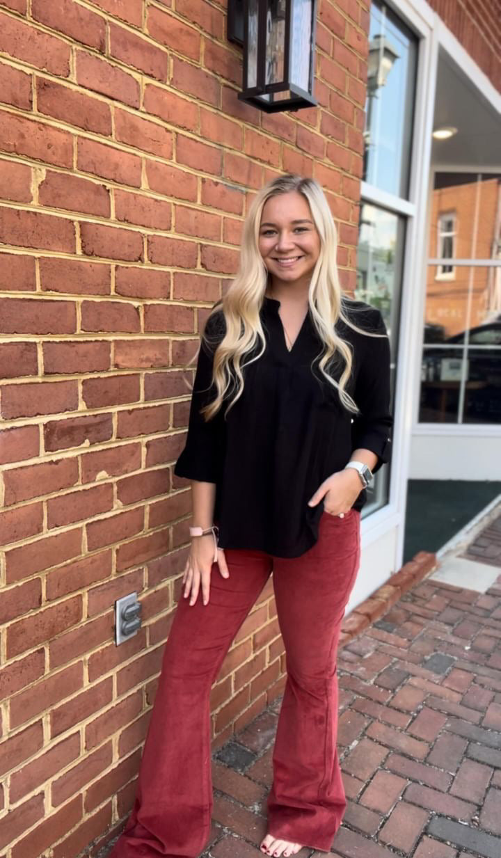 Brick wall and sidewalk. Woman wearing rust corduroy flare pants and black button up shirt uptucked.