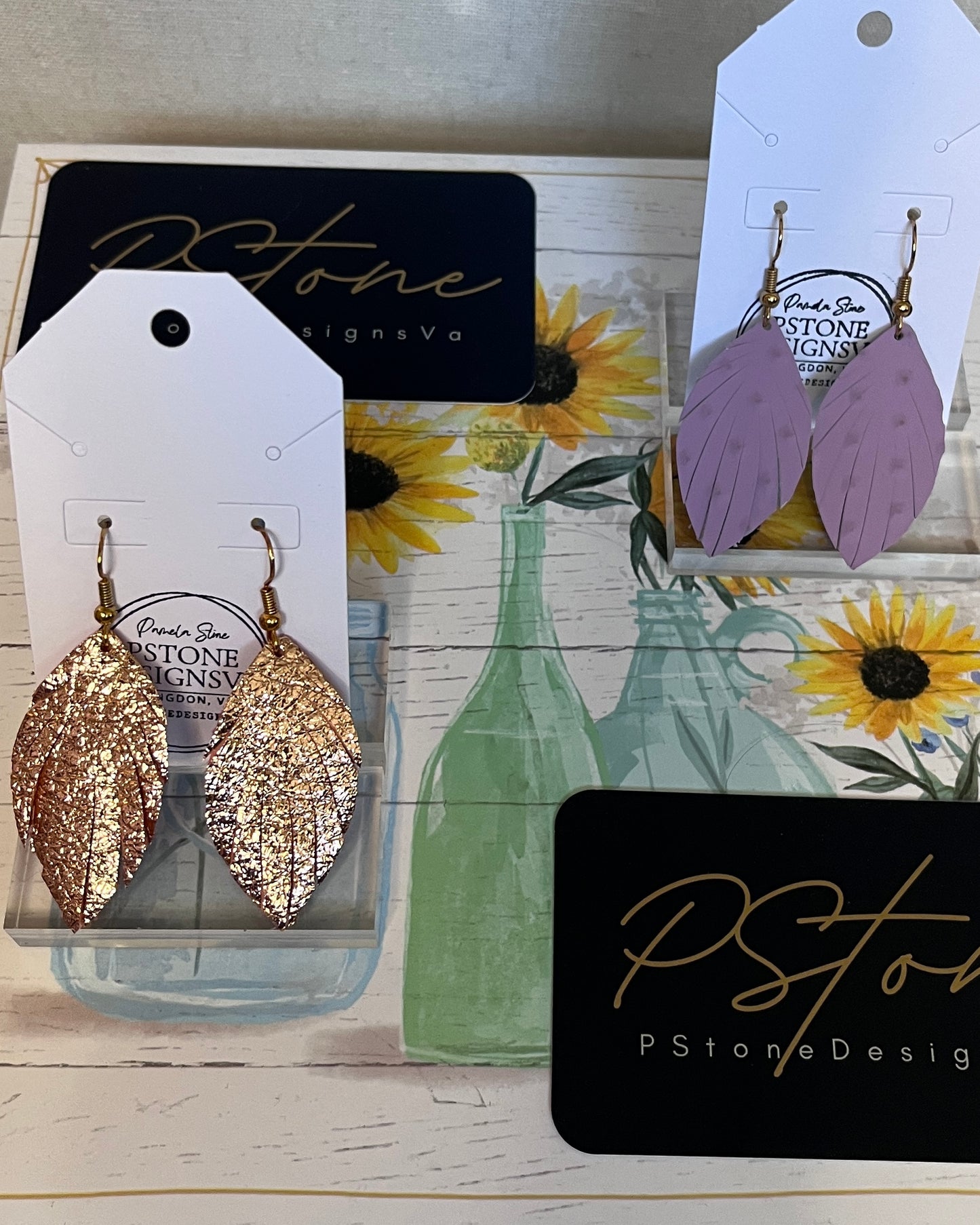 Gold and purple leaf-shaped earrings on P Stone Design cards with a floral background.
