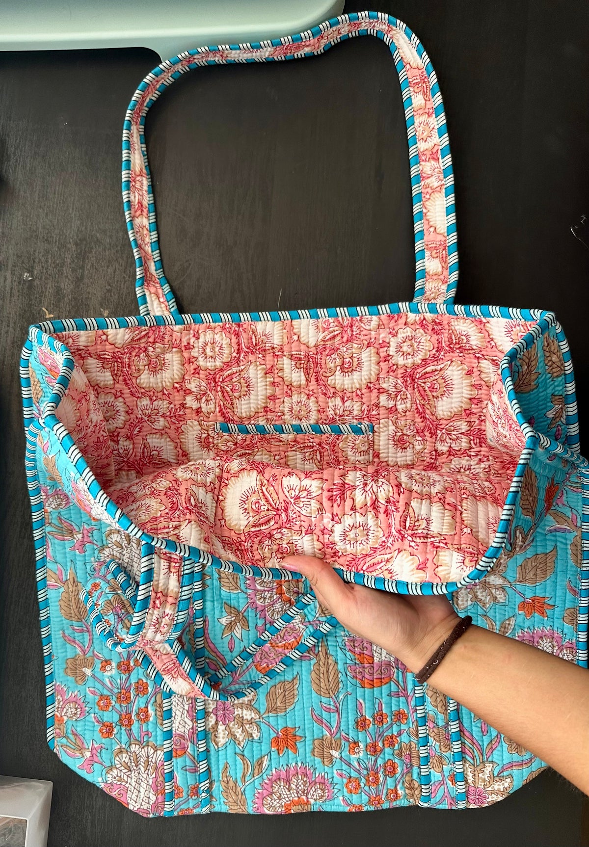 Handbag with floral pattern held by a hand against a dark background