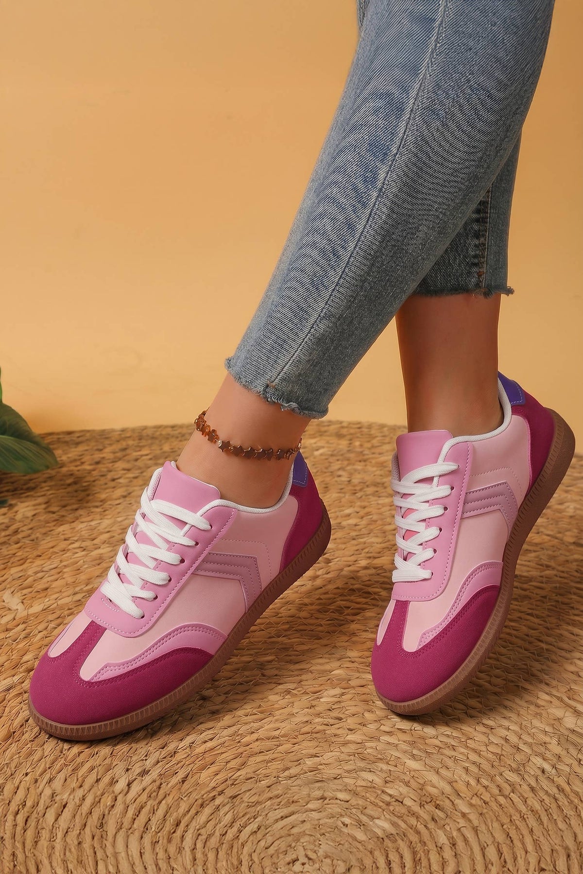 Pink and purple sneakers worn with blue jeans on a textured surface.
