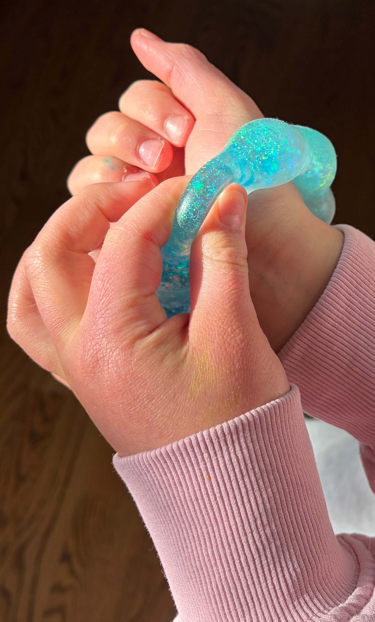 Close-up of hands holding a blue squishy bracelet against a wooden background.