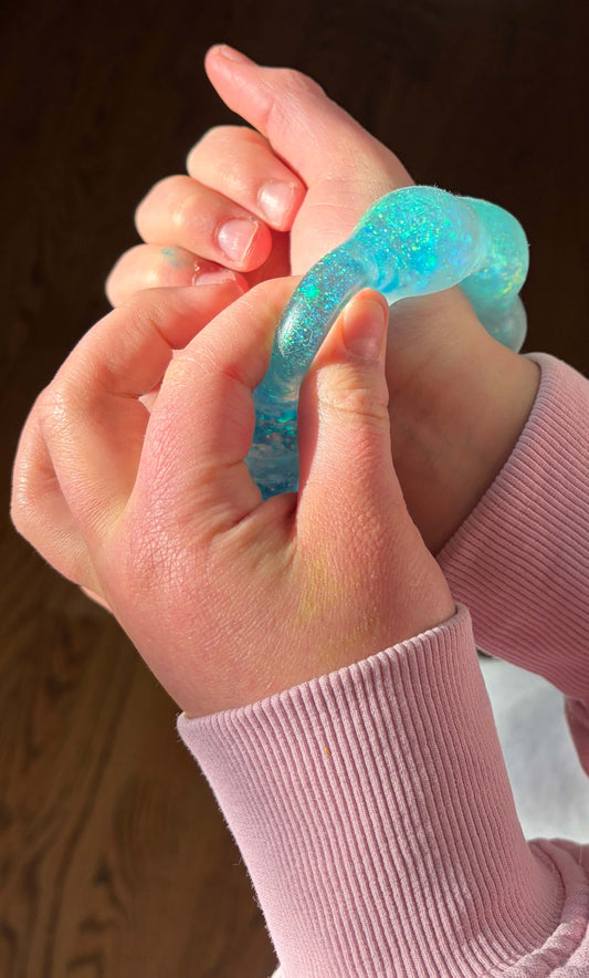 Close-up of hands holding a blue squishy bracelet against a wooden background.