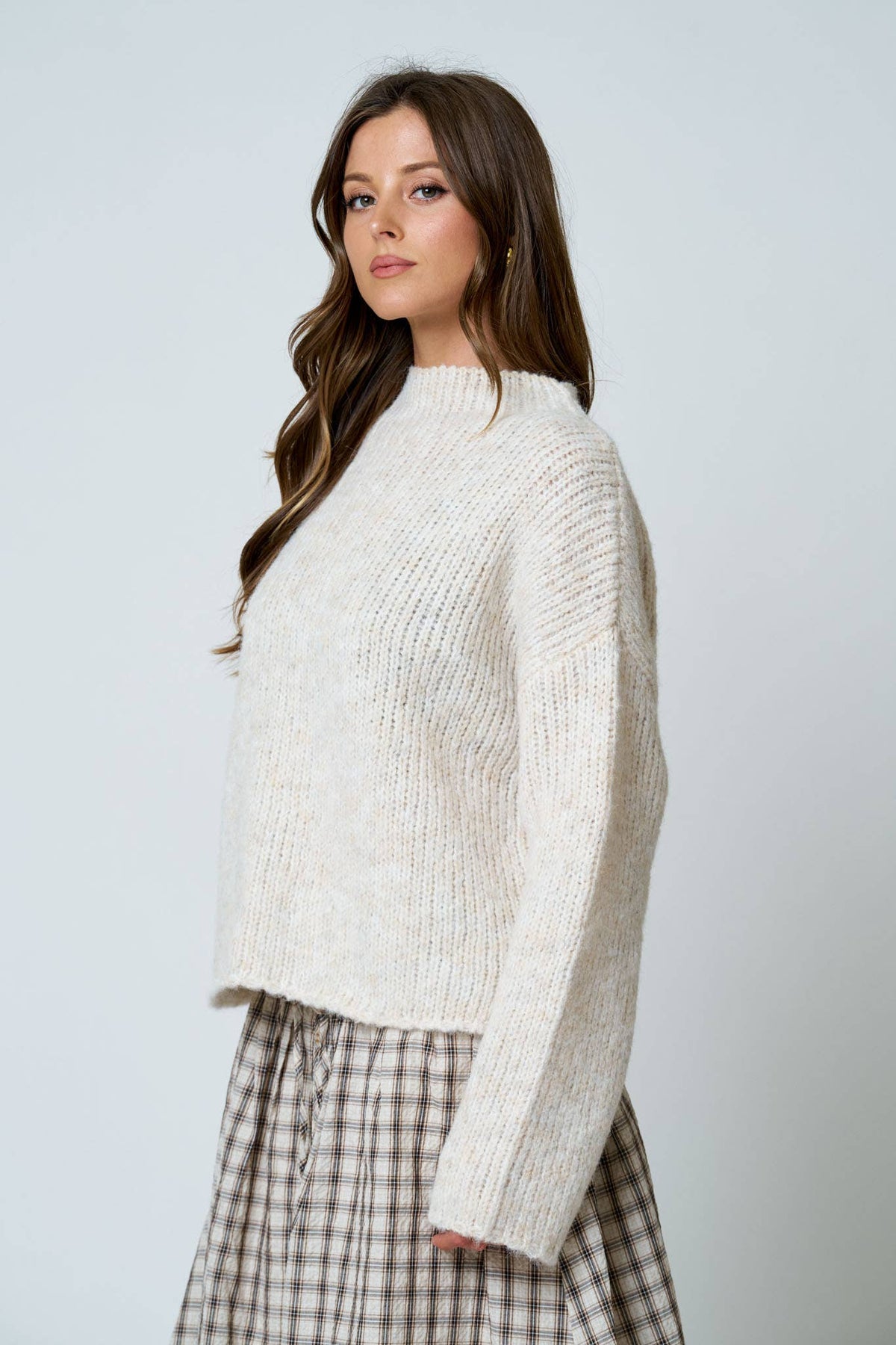Woman wearing a white sweater and plaid skirt on a light gray background