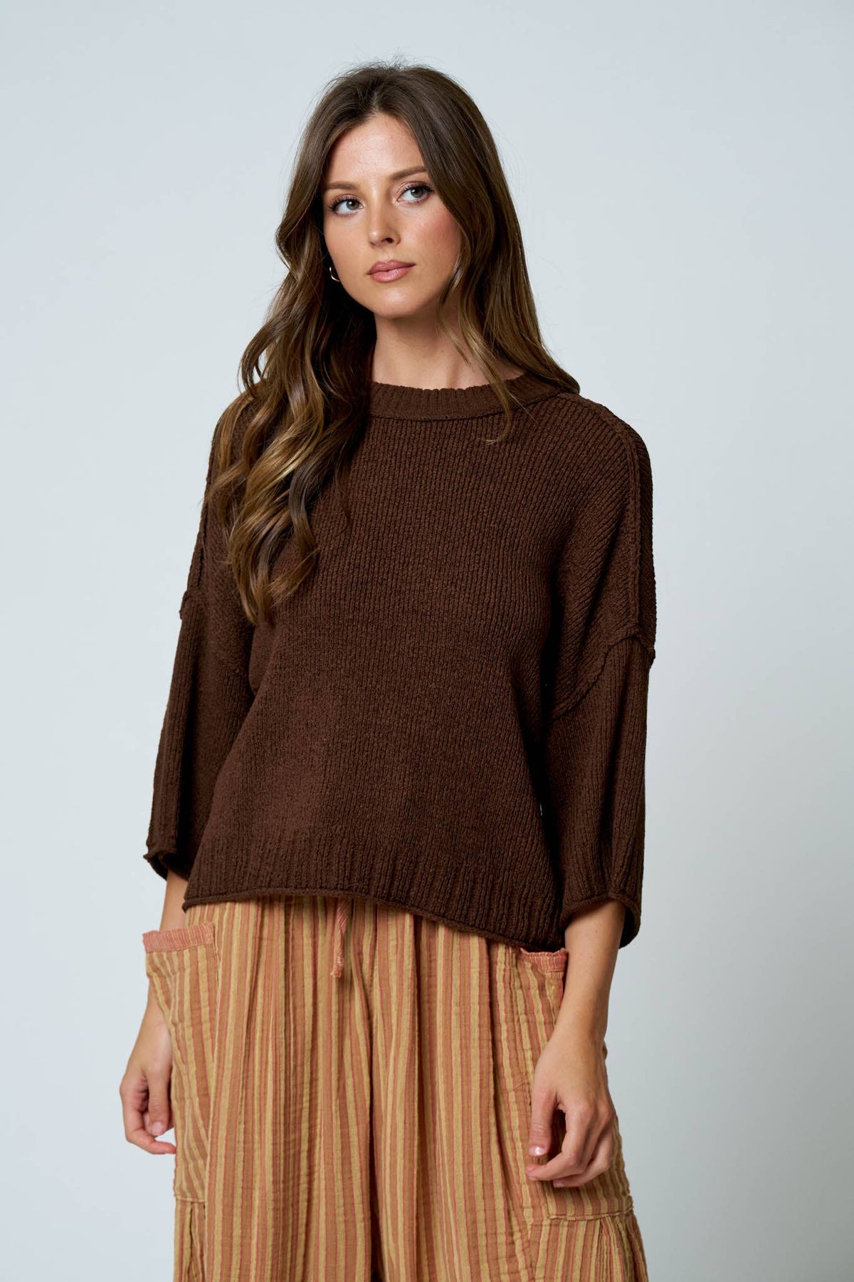 Woman wearing a brown sweater and beige pants against a white background