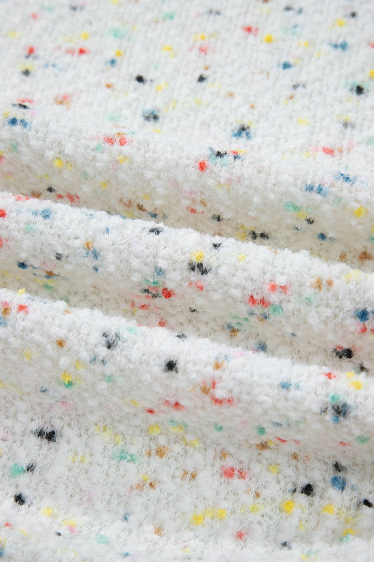 A close-up of a white cardigan with small scattered confetti-like specks in multiple colors including yellow, blue, red, black, and orange.