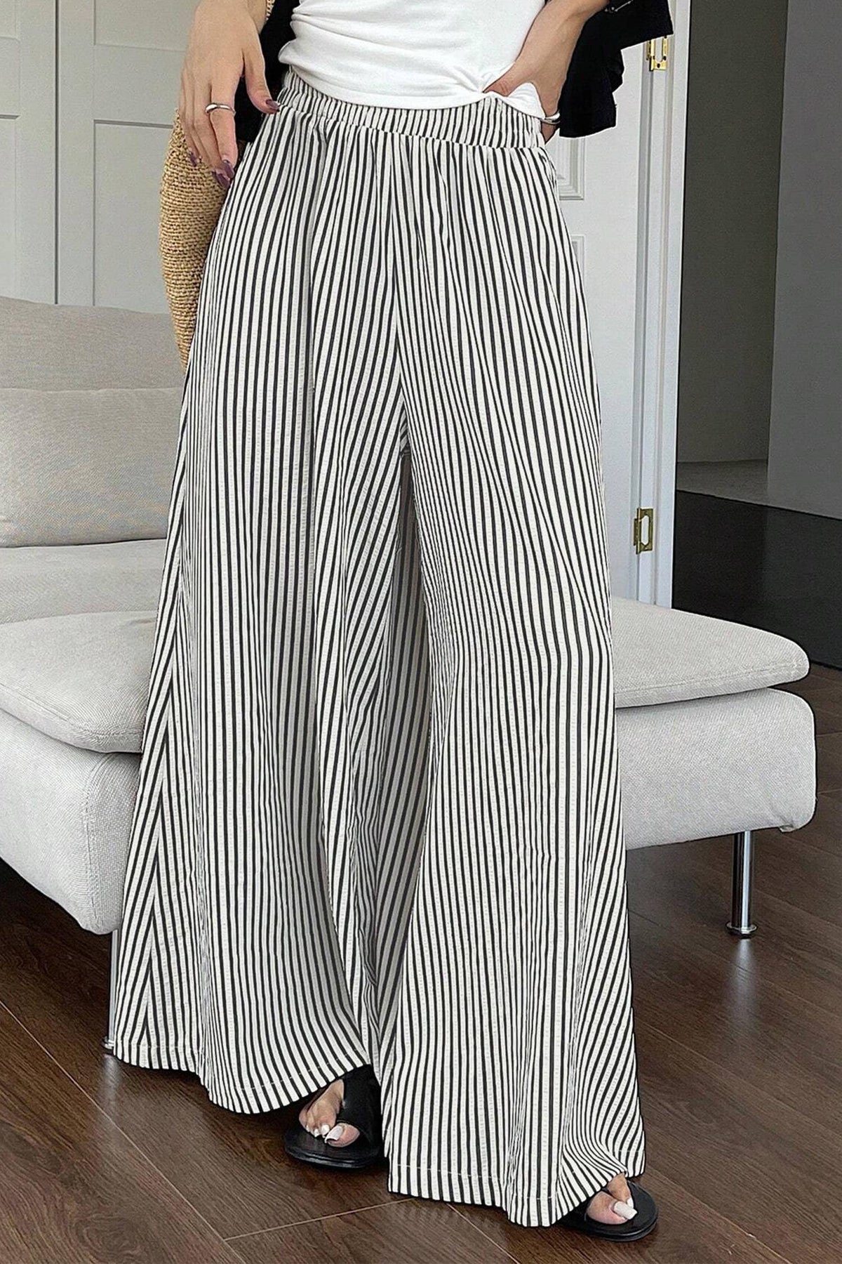 Person wearing black and white striped wide-leg pants in a room with a couch.