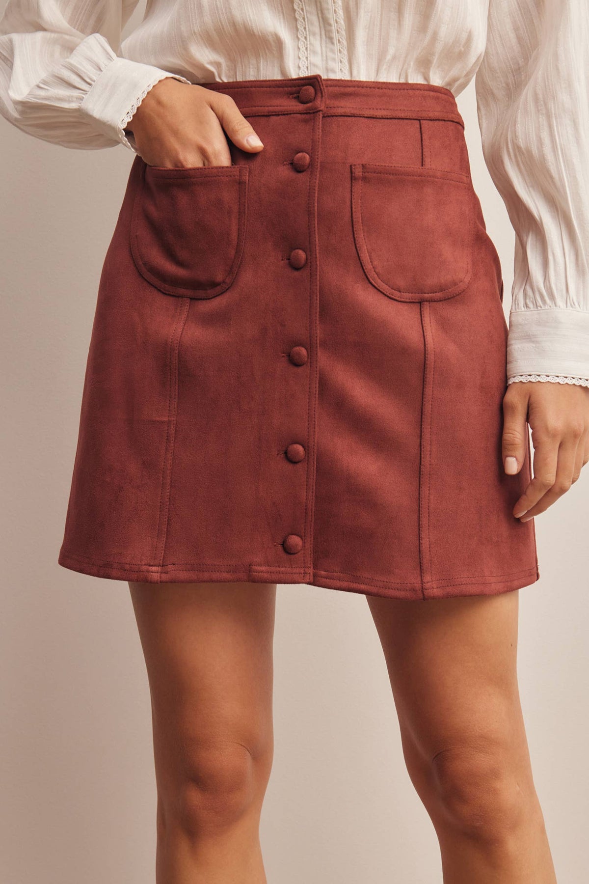 Person wearing a red skirt with buttons on a beige background