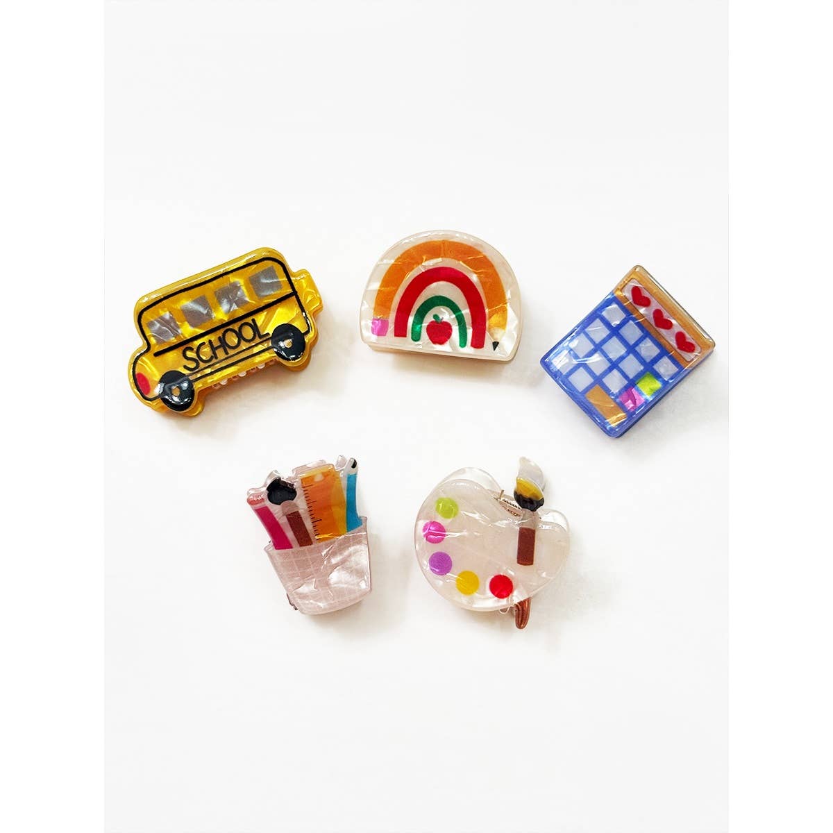 Set of colorful school themed hair clips including a school bus, rainbow, calculator, pencil holder, and paint palette on a white background.