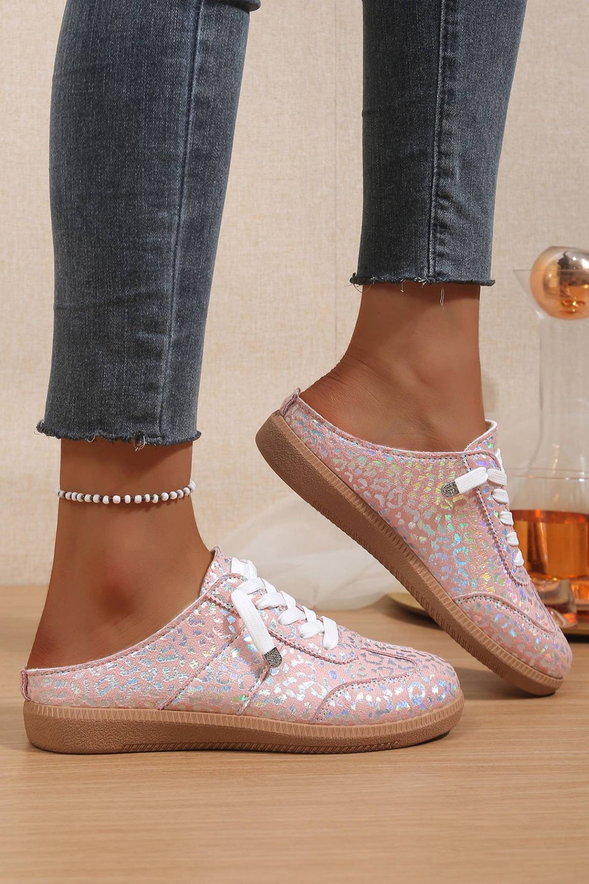 Woman trying on pink glittery leopard sneakers with white laces on a wooden floor.