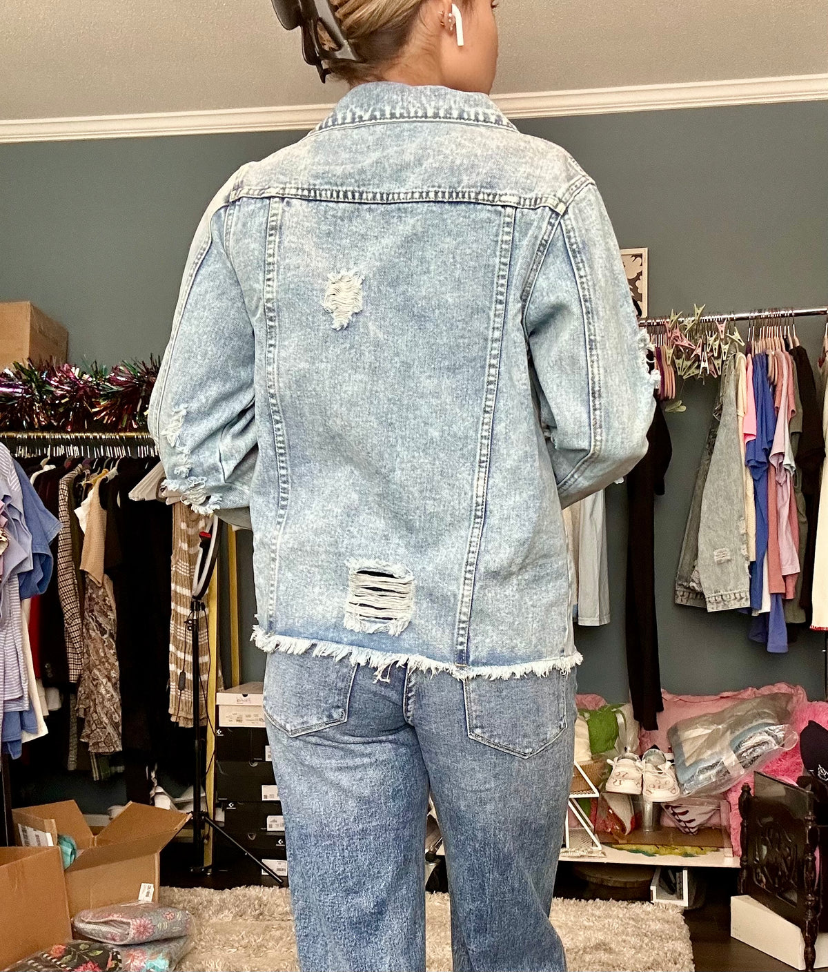 Person wearing a distressed denim jacket and jeans in a clothing store.