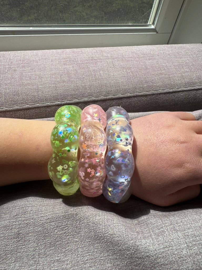 Three colorful squishy bracelets on a person's wrist with a neutral background