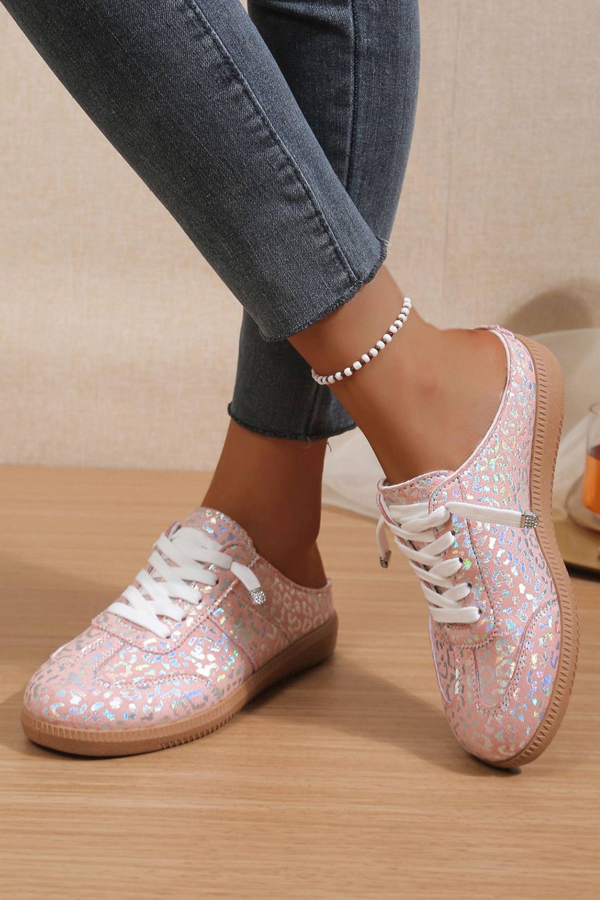 Woman trying on pink glittery leopard sneakers with white laces on a wooden floor.