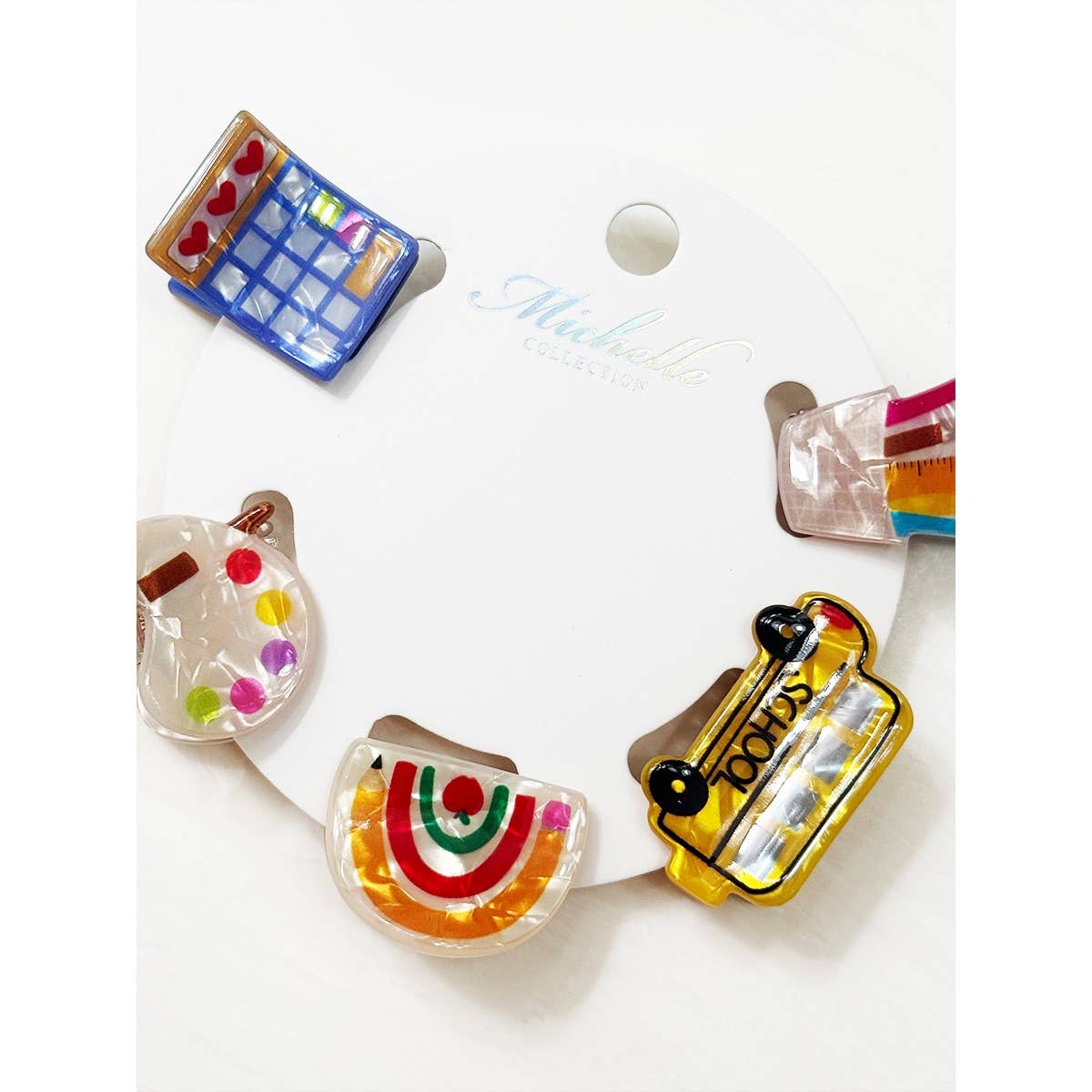 Set of colorful school themed hair clips including a school bus, rainbow, calculator, pencil holder, and paint palette on a white background.