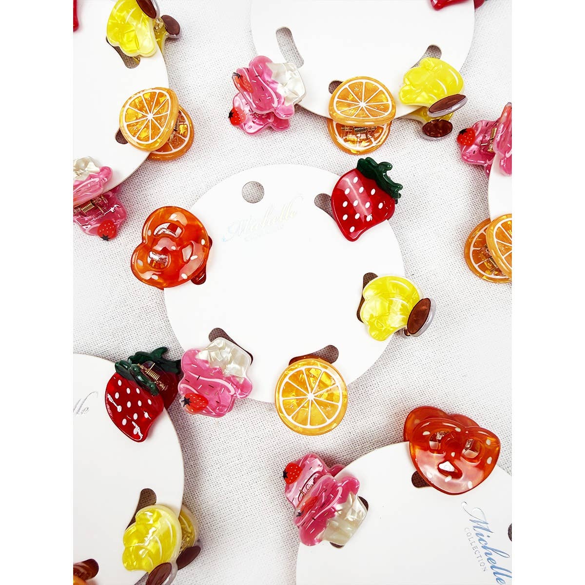 Colorful fruit-shaped hair clips on a white background. designs include strawberries, lemons, oranges, pretzels, and cupckes.