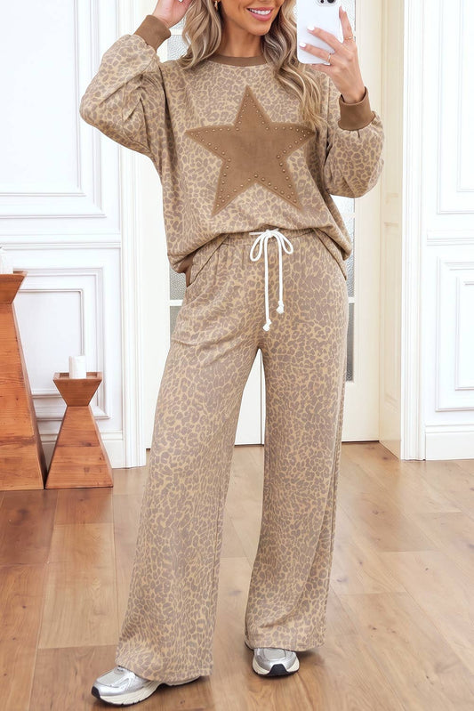 A woman modeling a matching beige and brown animal print lounge set, featuring a long-sleeve sweatshirt with a large star on the chest and matching wide-leg sweatpants with a white drawstring, standing in a room with light wood floors and white paneled walls.