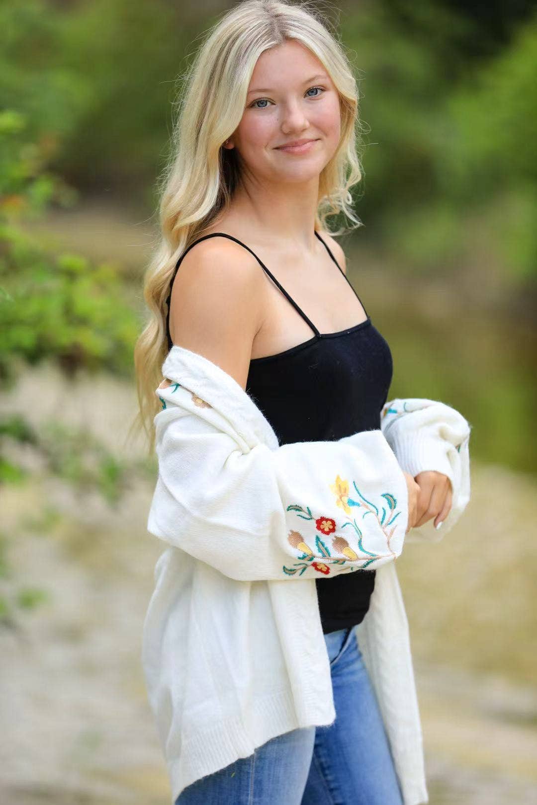 Woman wearing a black top and white embroidered cardigan outdoors