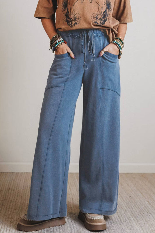 Person wearing blue wide-leg jeans and a brown shirt with a tattoo design, standing against a plain background.