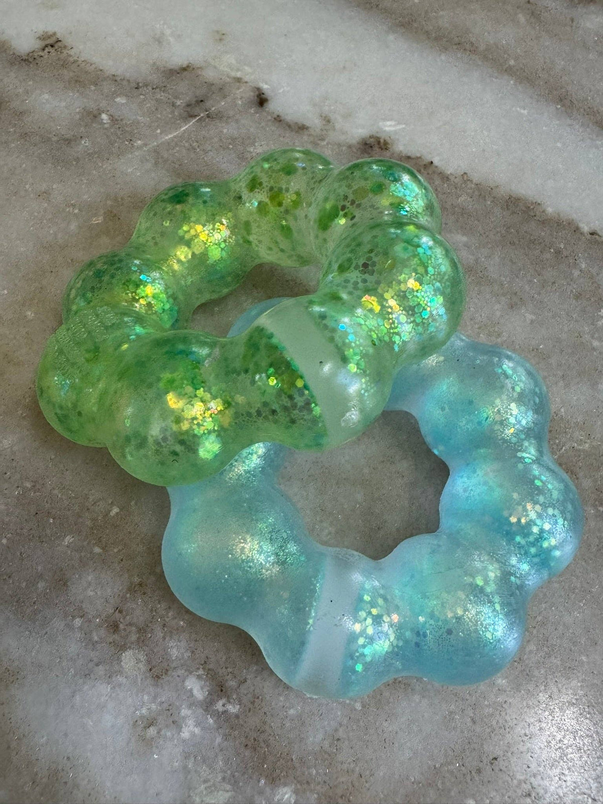 Two squish bracelets in green and blue on a concrete surface