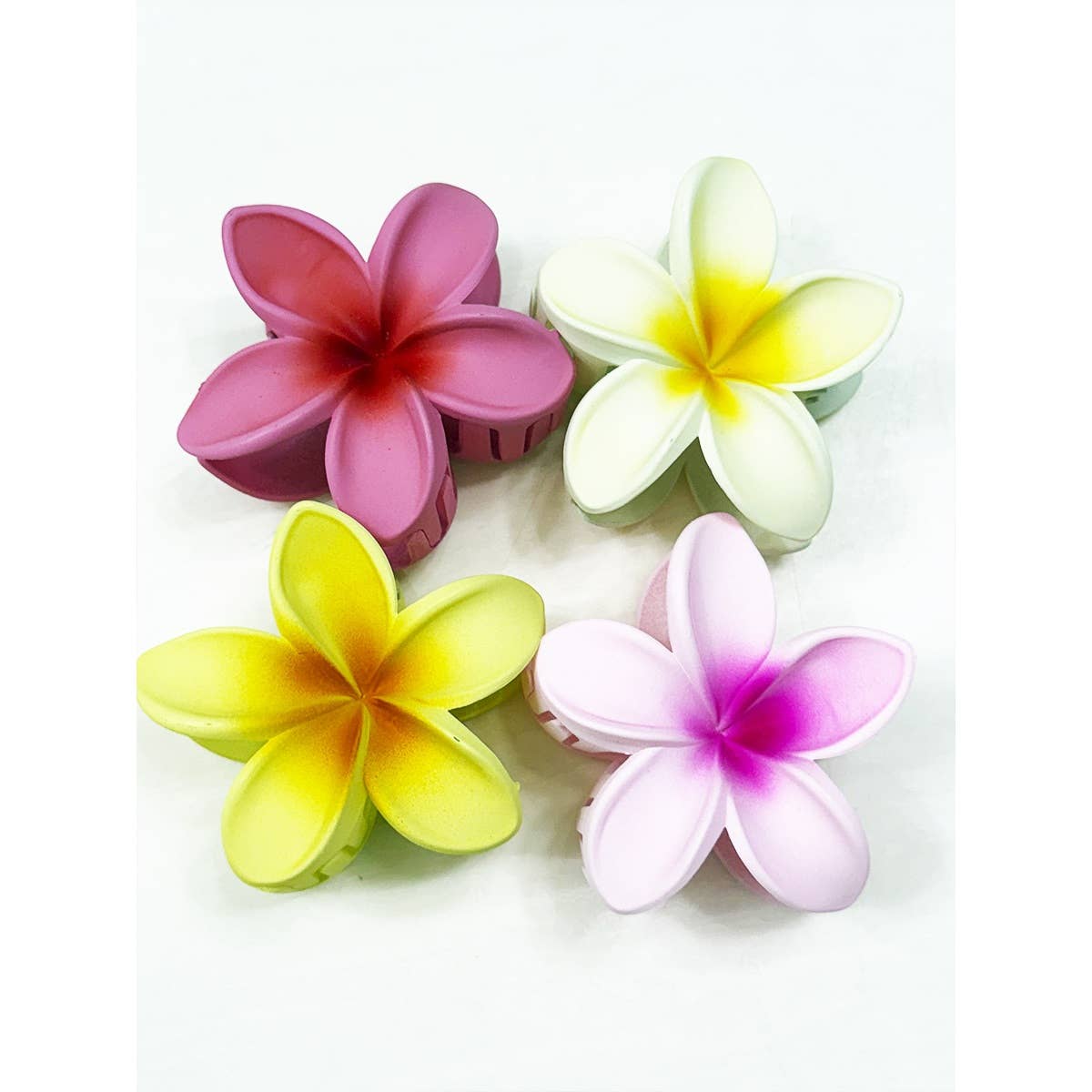 Four flower-shaped hair clips in pink, yellow, and white on a white background