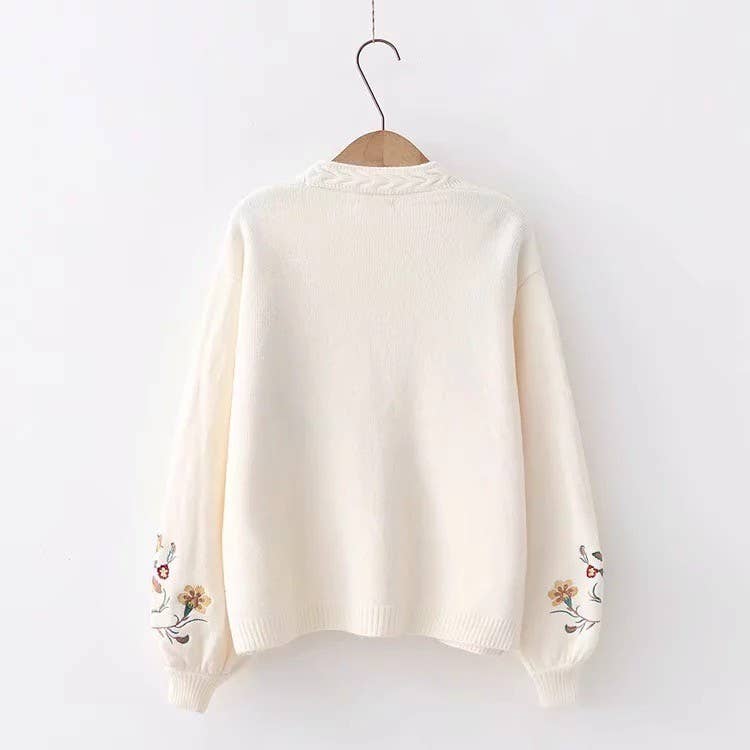 White sweater with floral embroidery on a wooden hanger against a white background