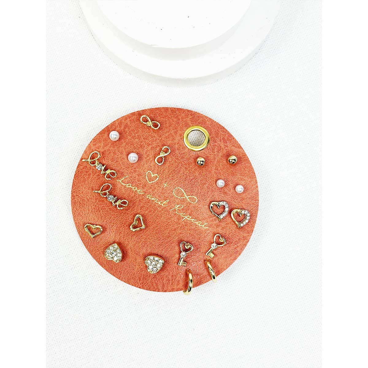 Round orange earring display card with various earrings on a white background