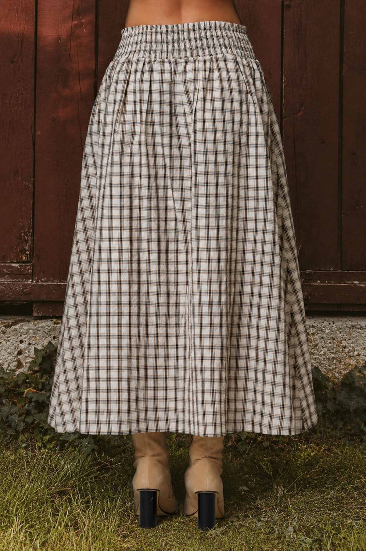 Person wearing a long checkered skirt in front of a wooden fence.