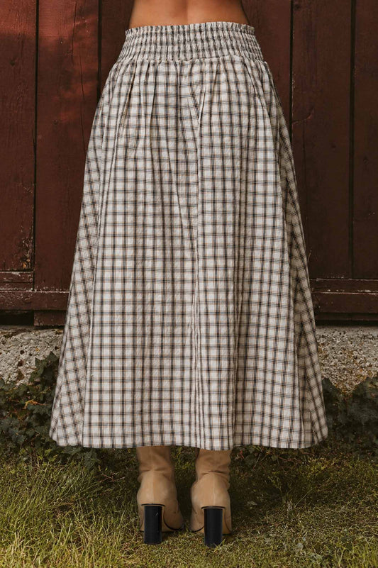 Person wearing a long checkered skirt in front of a wooden fence.