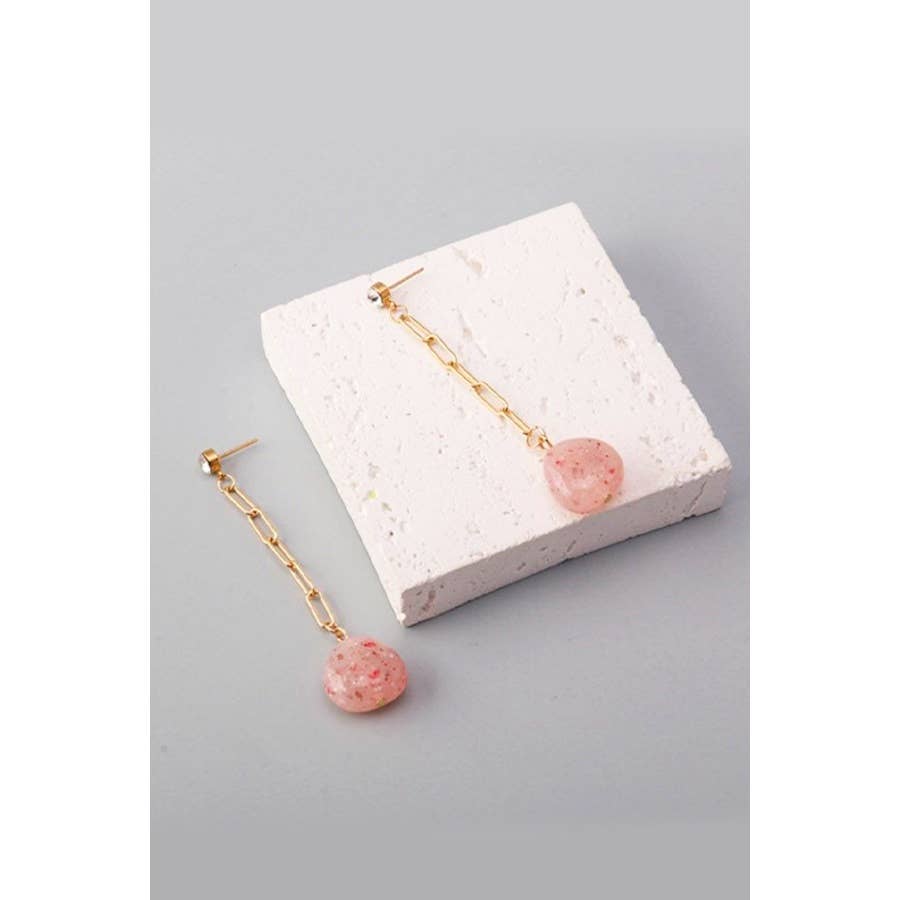 Pair of pink earrings with gold chains on a gray surface