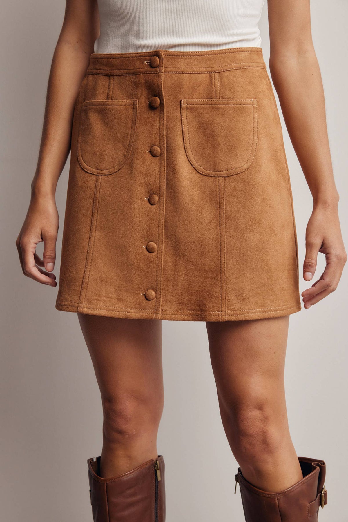 Brown suede skirt with button details worn by a person on a neutral background