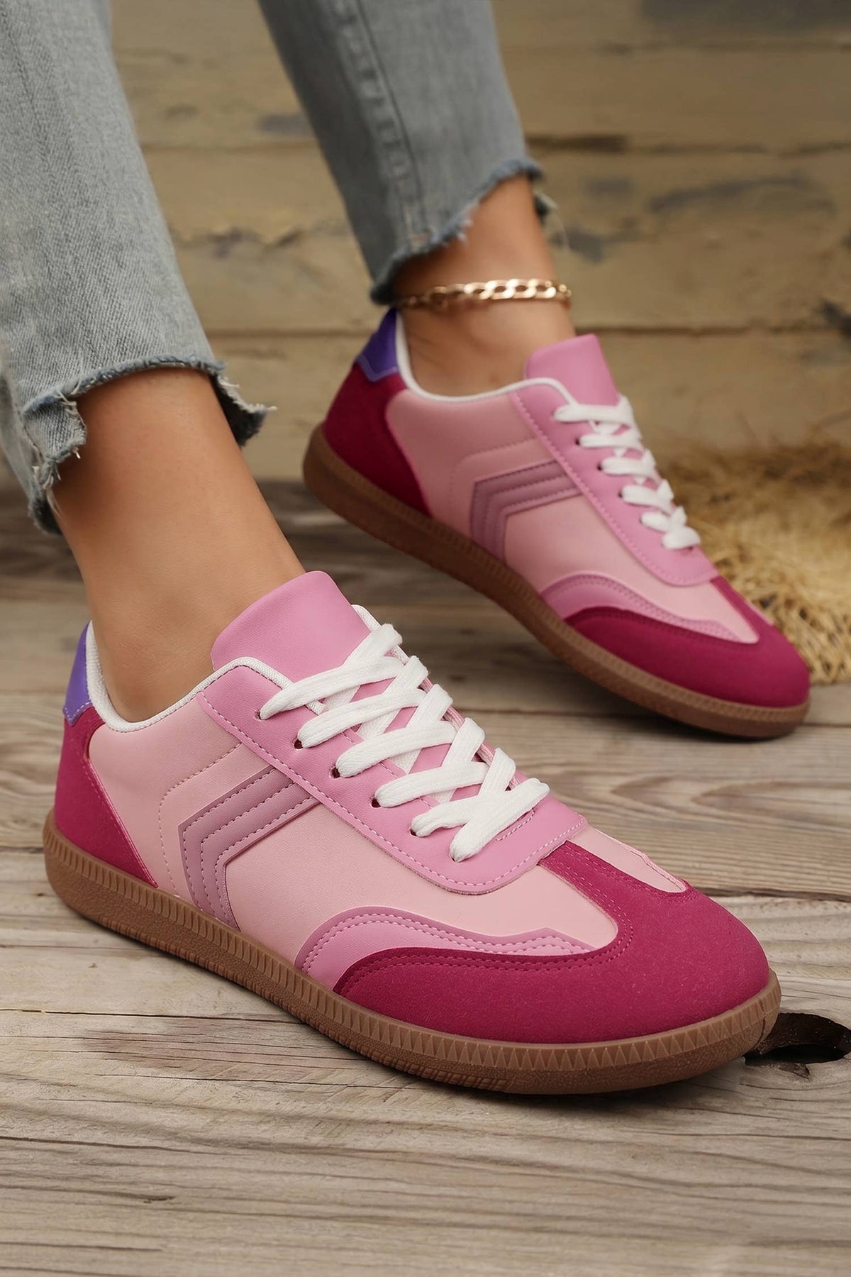 Pink and red sneakers with white laces on a wooden floor.
