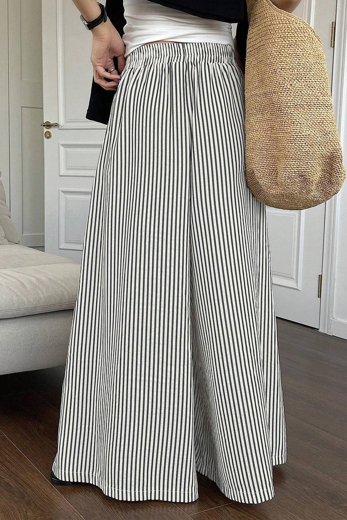 Person wearing a black and white striped wide-leg pants with a beige bag indoors.