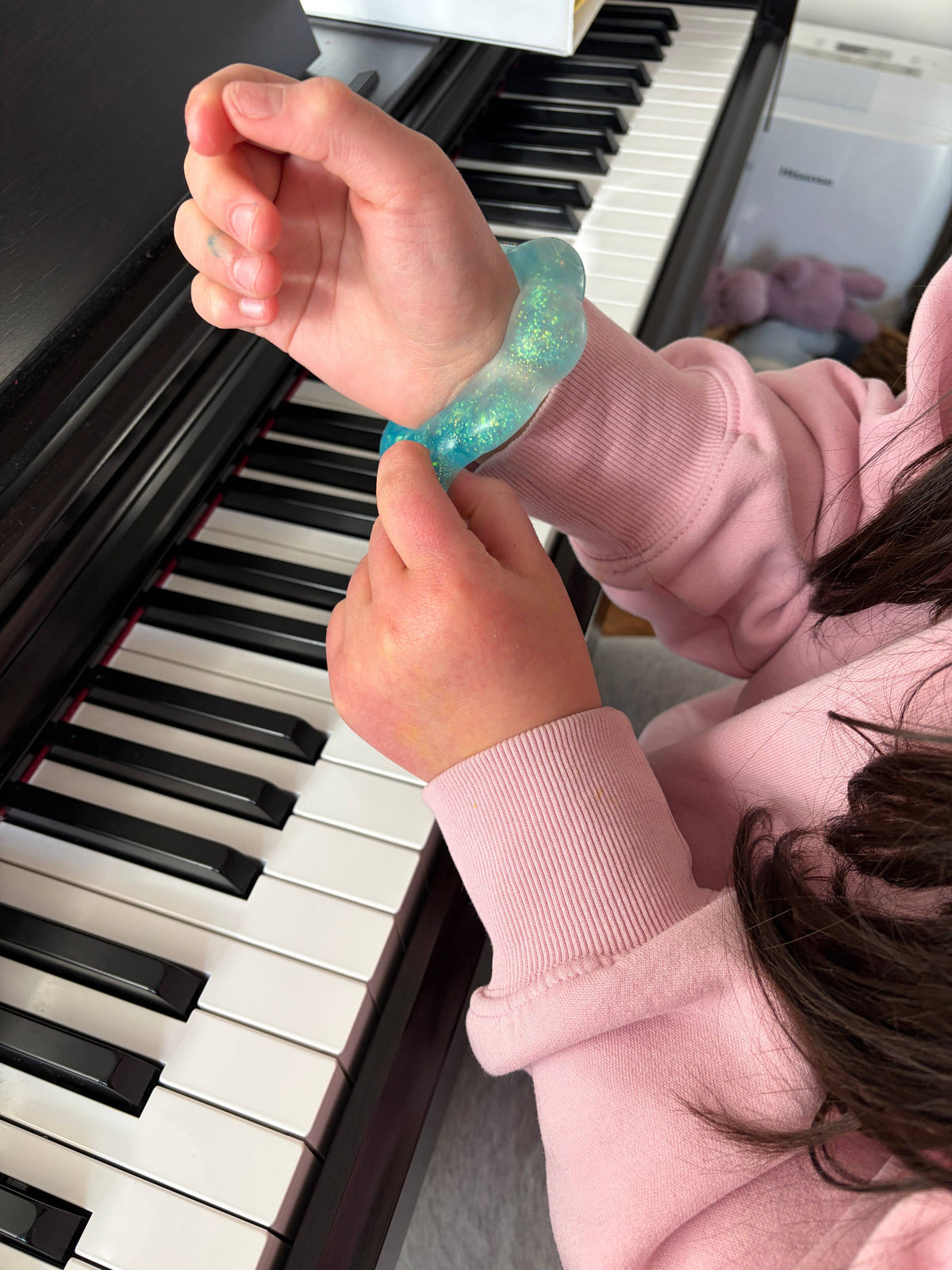 Child's hand wearing a blue squishy bracelet on a piano keyboard