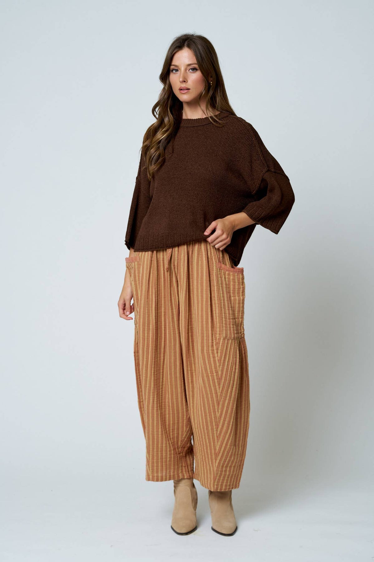Woman wearing a brown sweater and tan striped pants on a white background