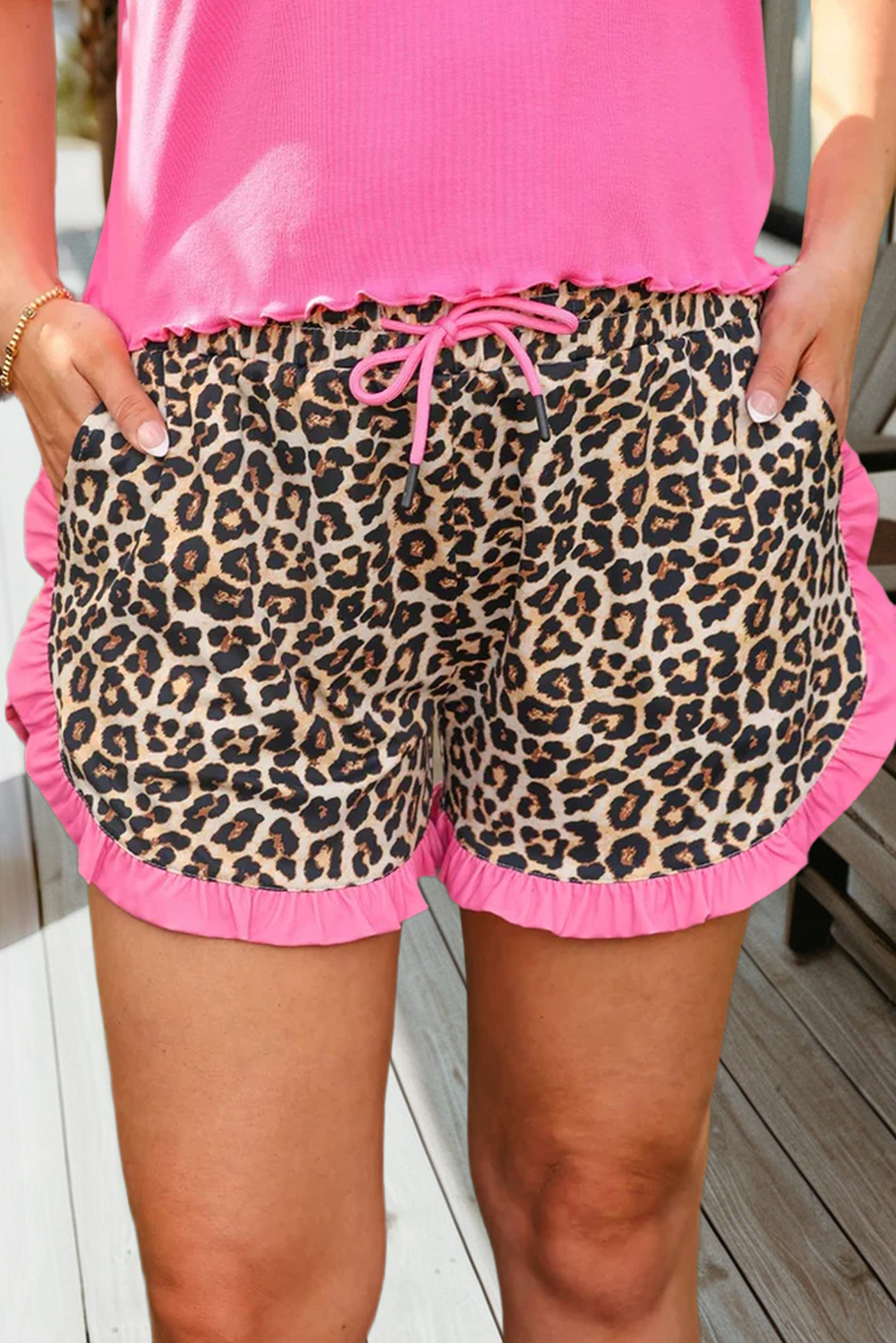 Leopard print shorts with pink trim worn by a person on a wooden deck.