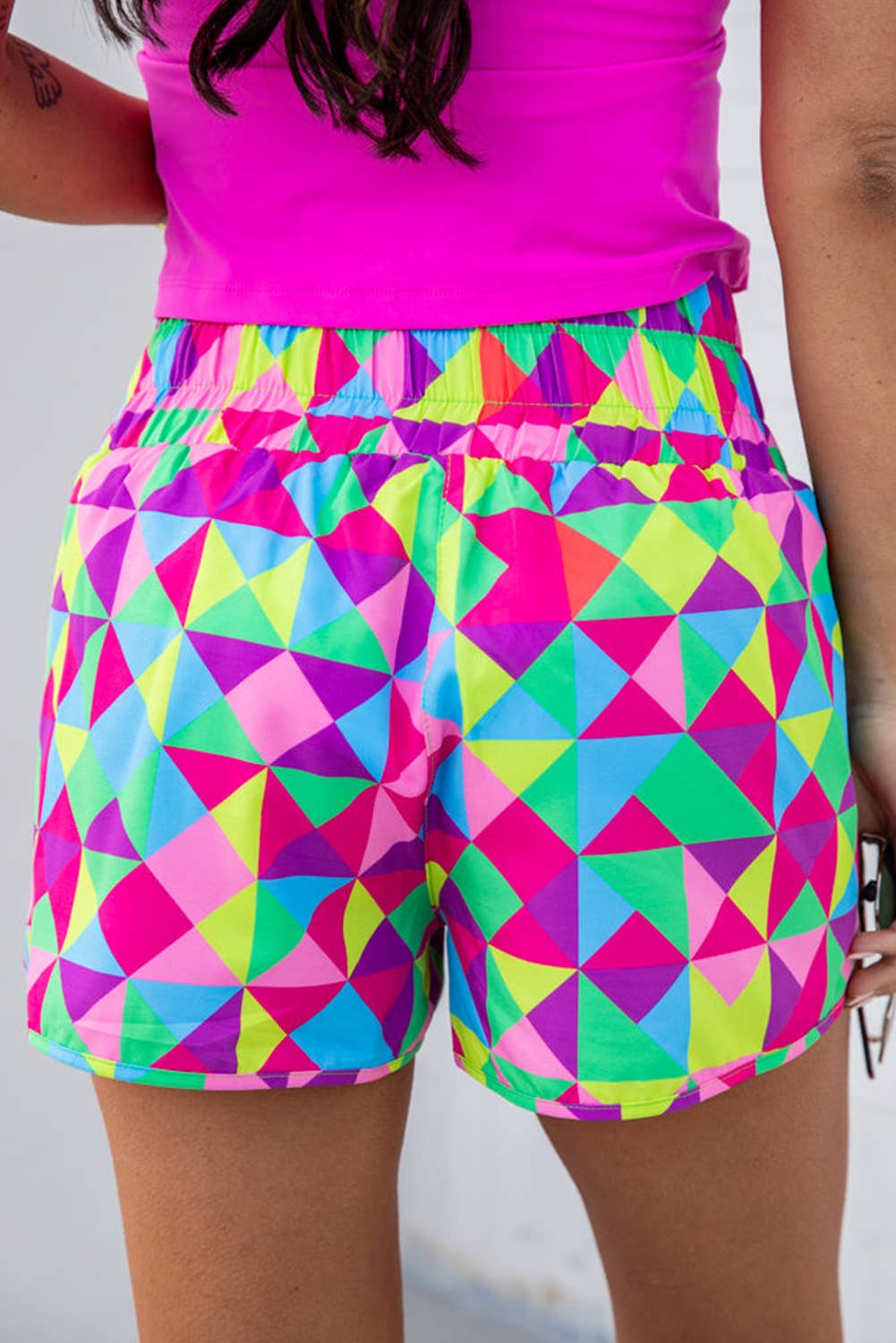 Person wearing bright pink top and colorful geometric shorts on a plain background