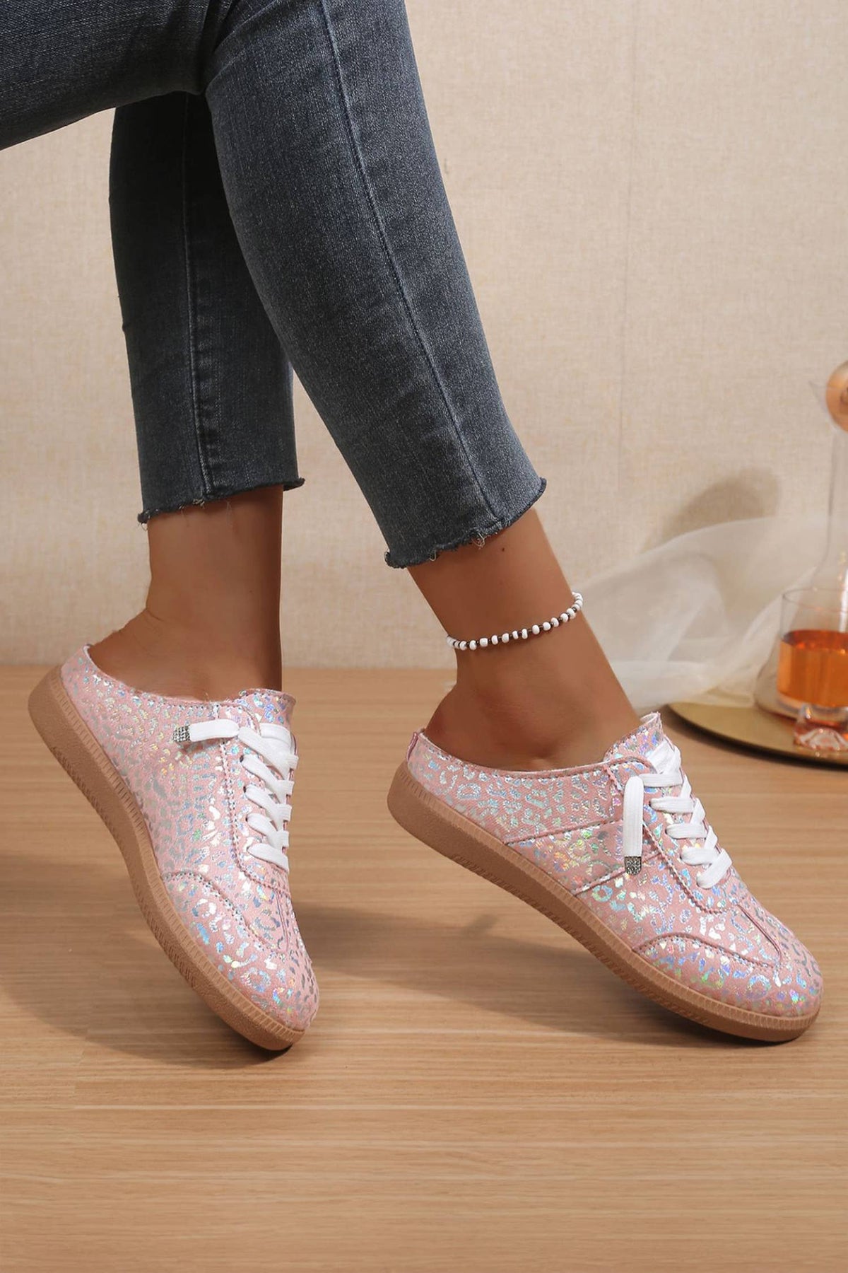 Woman trying on pink glittery leopard sneakers with white laces on a wooden floor.