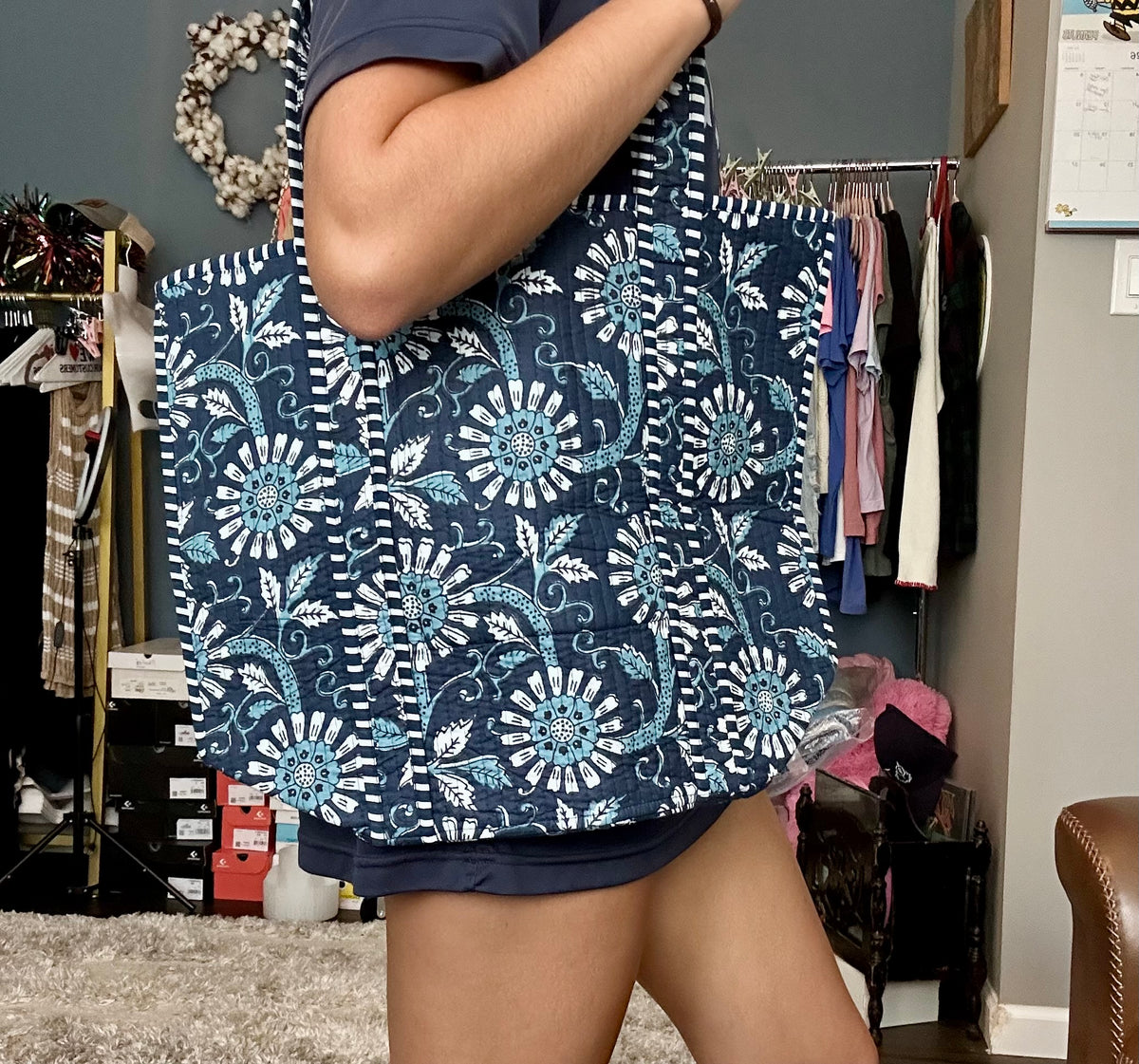 Person holding a large blue and white floral tote bag in a room with clothing racks.