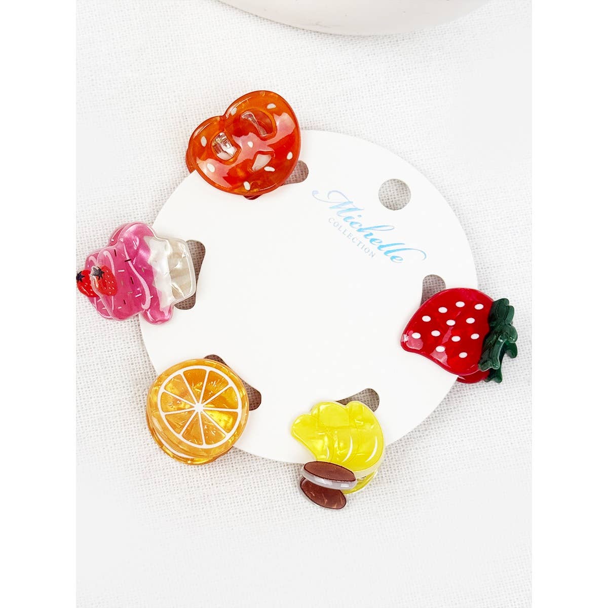 Colorful fruit-shaped hair clips on a white card with 'Michelle' branding.