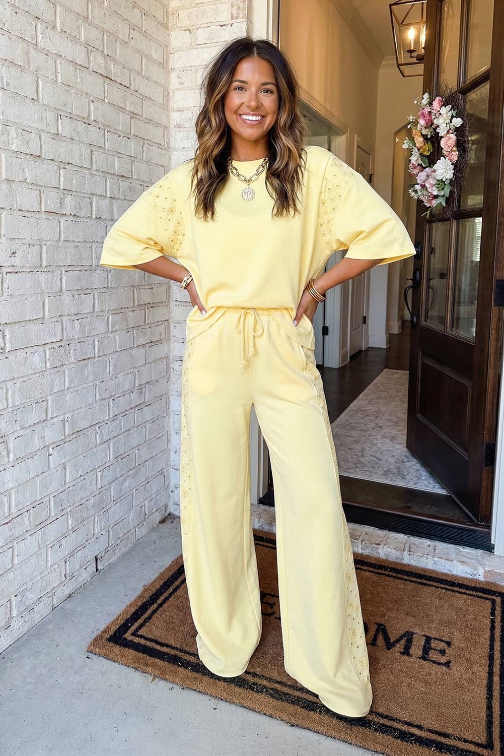 Woman in a yellow outfit standing on a porch with a white brick wall and door in the background.