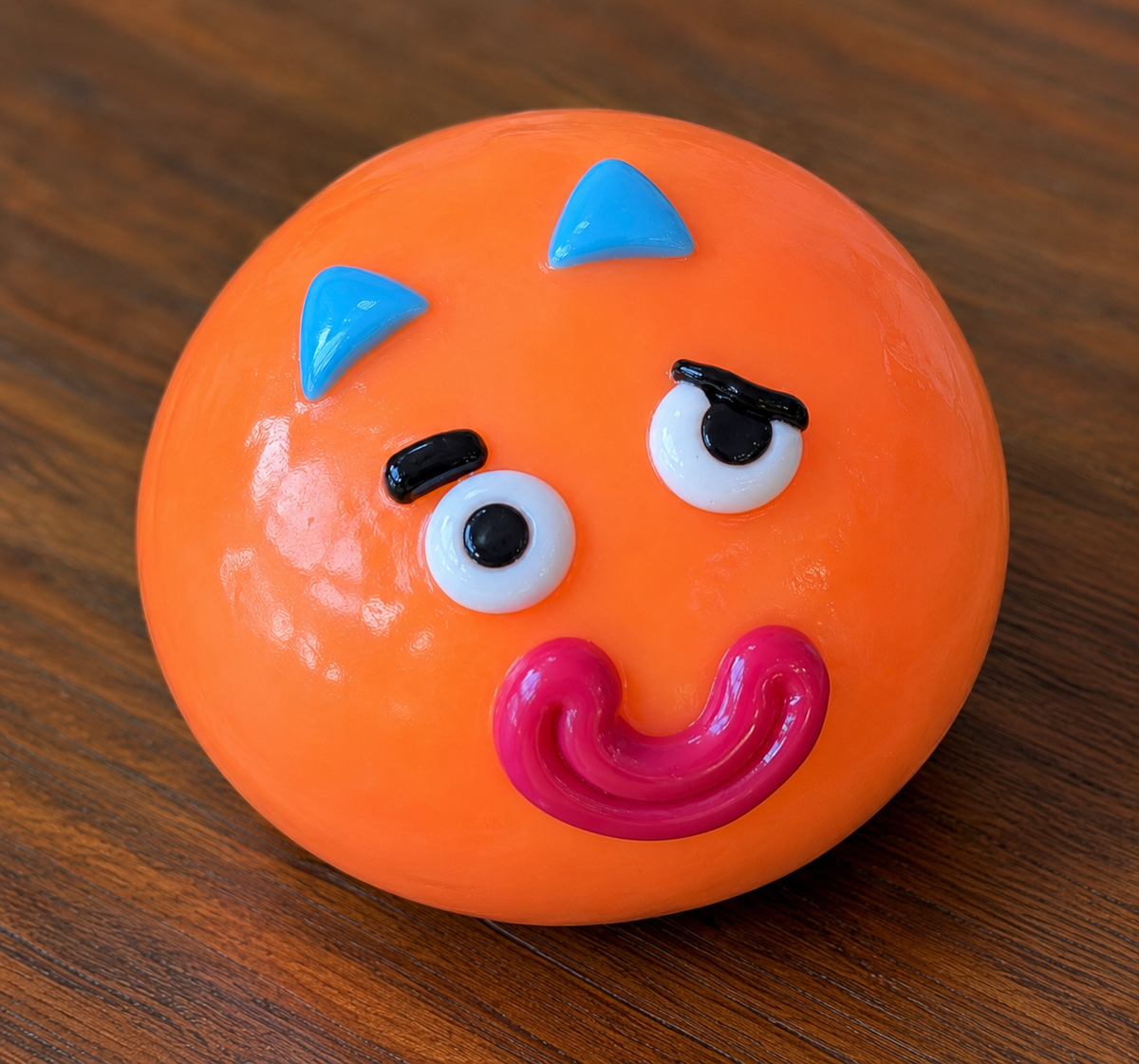 Orange squish ball with a face on a wooden surface