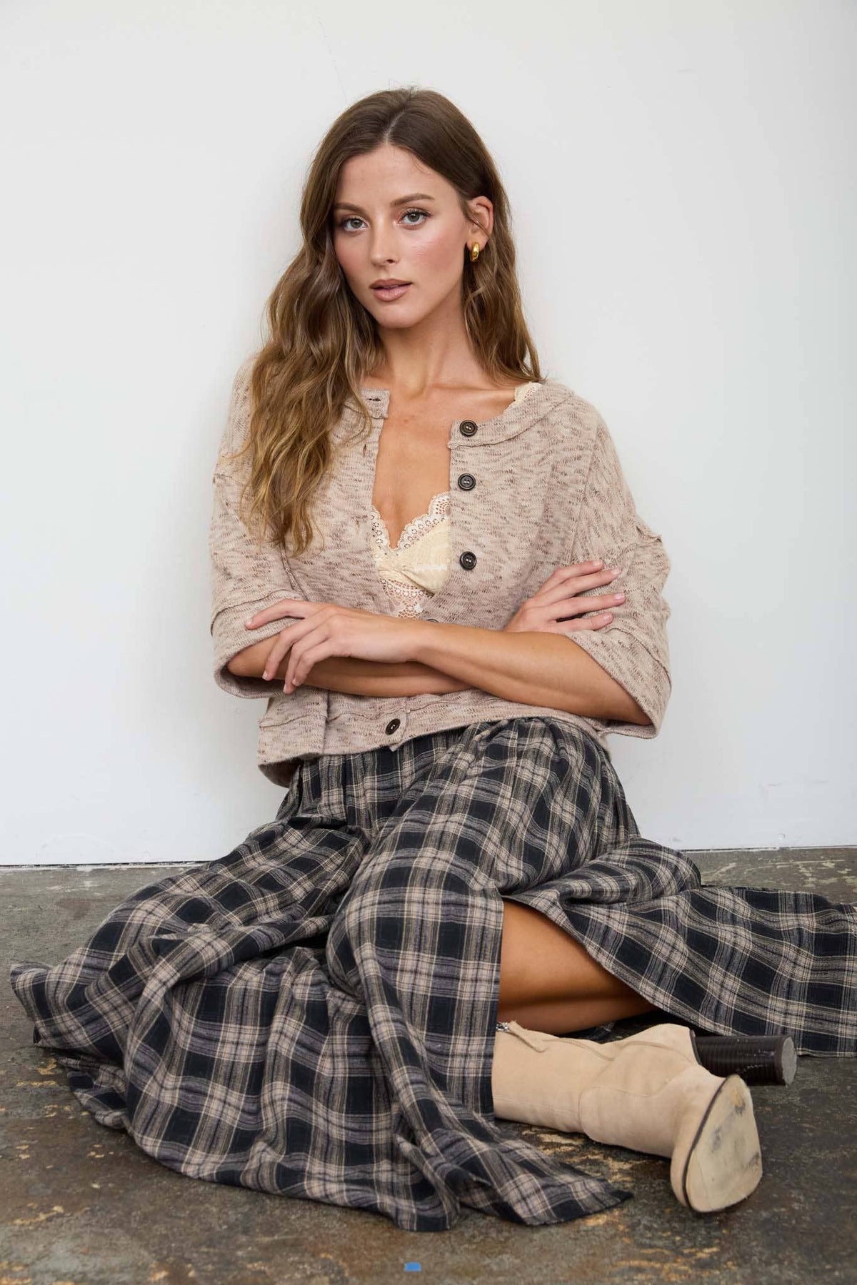 Woman wearing a beige sweater and plaid skirt sitting against a white wall.