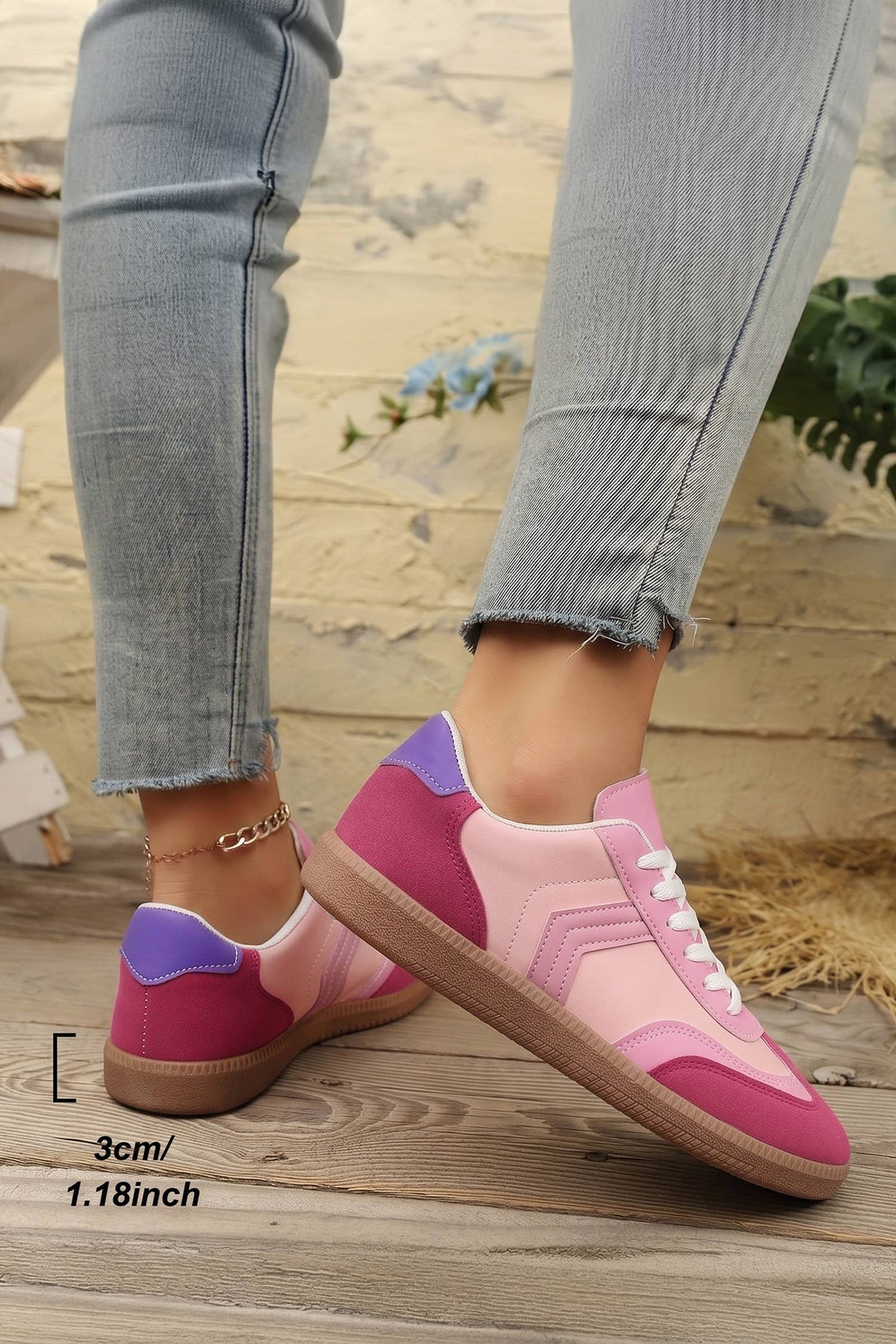 Pink and purple sneakers worn with light blue jeans on a wooden floor.