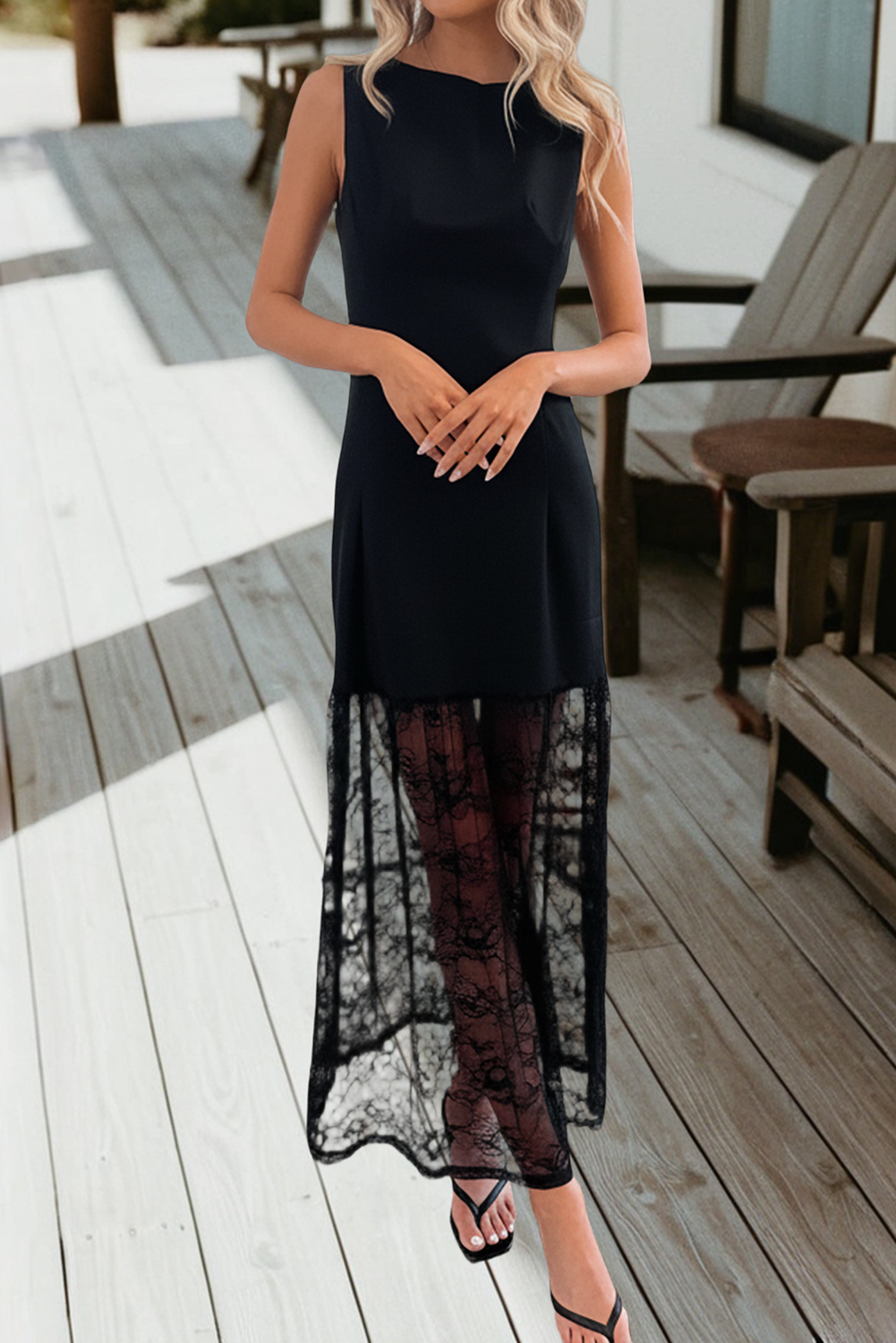 A woman wearing a sleeveless black midi dress with a sheer black lace overlay skirt, standing on a light-colored wooden deck.