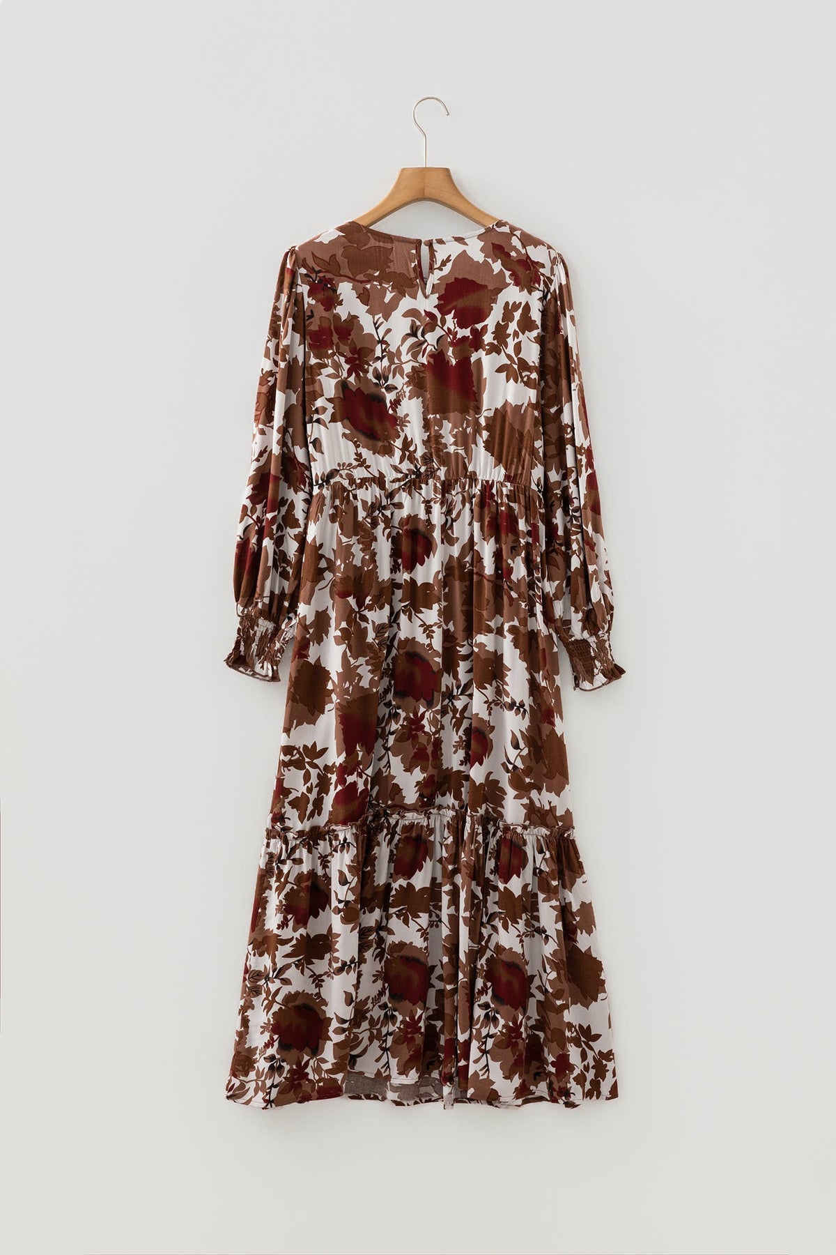 A long-sleeved midi dress with a brown and white floral pattern, hanging on a wooden hanger against a light gray wall.