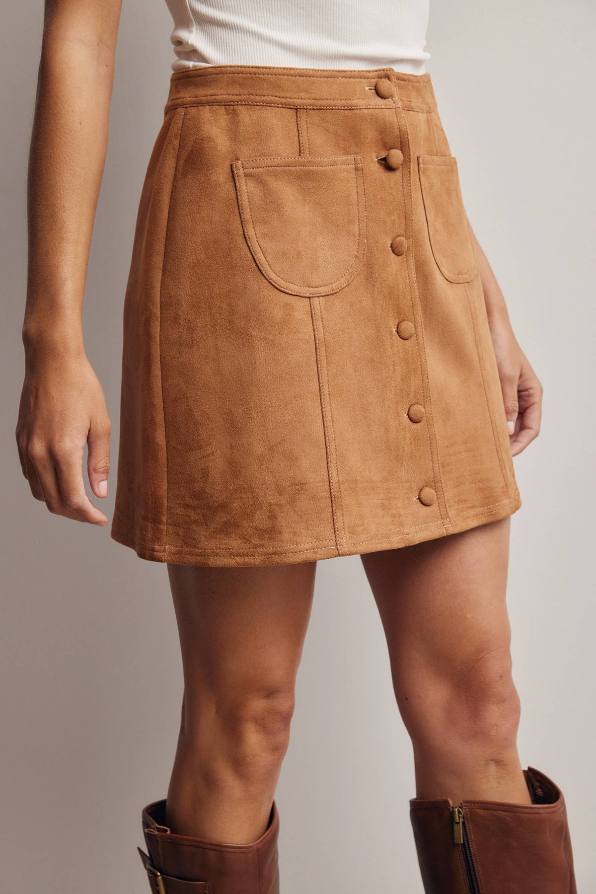Brown suede skirt with button details worn by a person on a plain background
