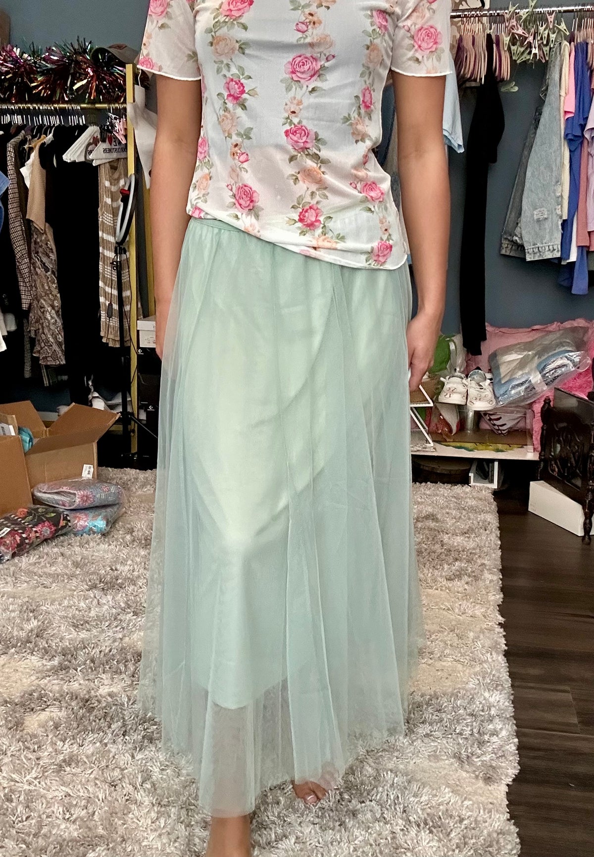 Person wearing a floral top and light green skirt in a clothing store.