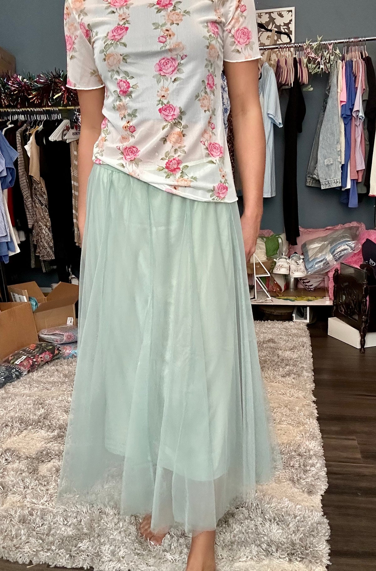 Person wearing a floral top and light green skirt in a clothing store.