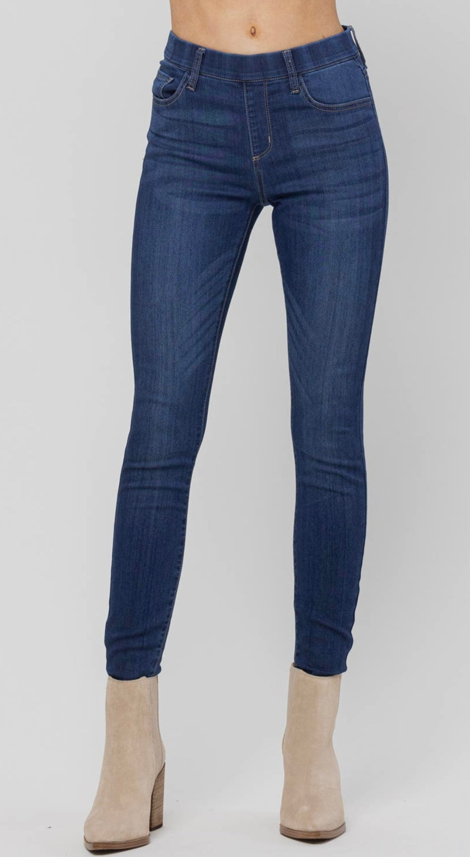 Woman modeling mid rise, pull-on skinny jeans in dark wash with beige booties.