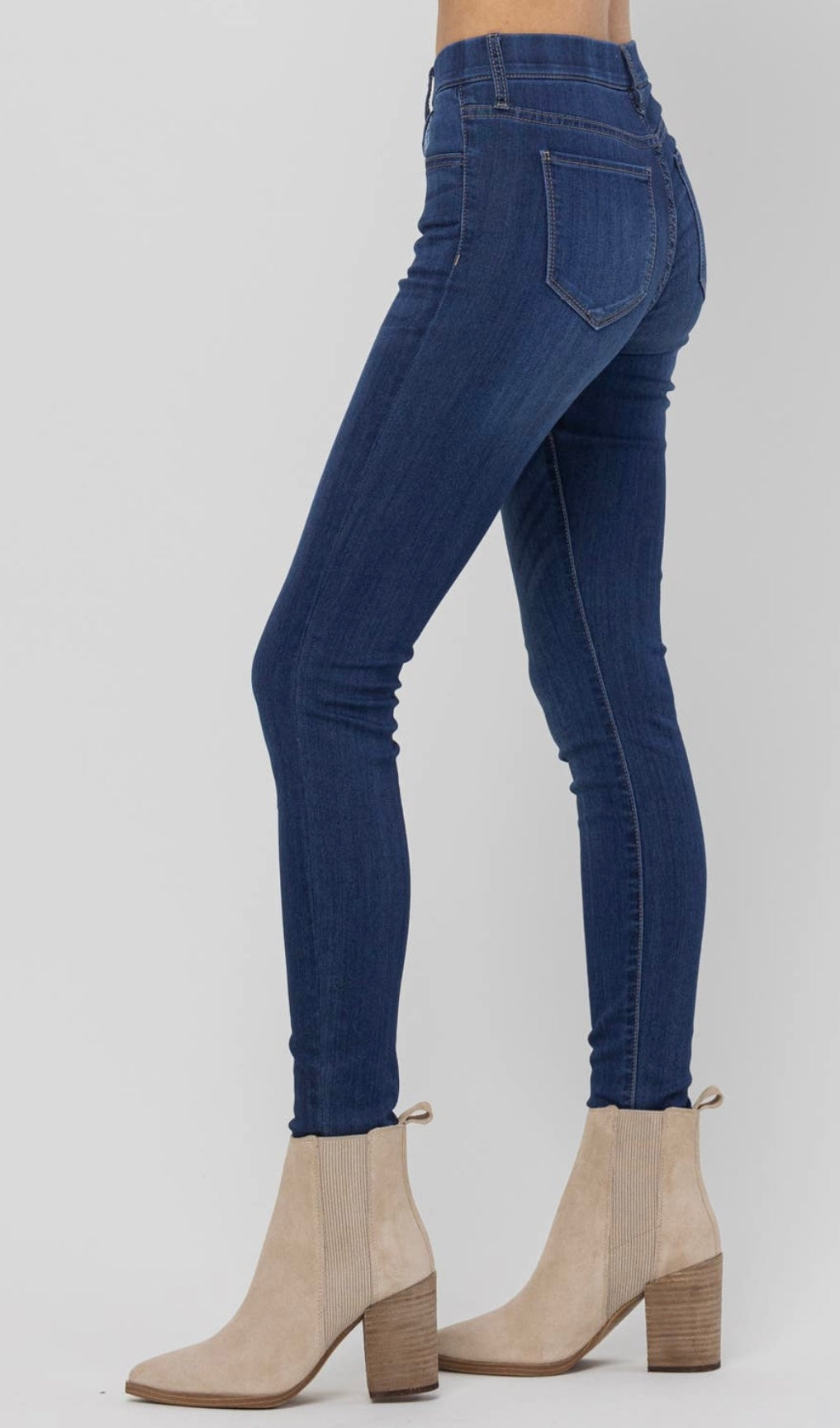 Woman modeling mid rise, pull-on skinny jeans in dark wash with beige booties.